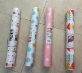 Four rolls of kitchen wrapping paper laid out on a beige tiled floor. The rolls feature different patterns: strawberry and daisy prints, blue polka dots, white polka dots, and a red, yellow, and green geometric pattern.