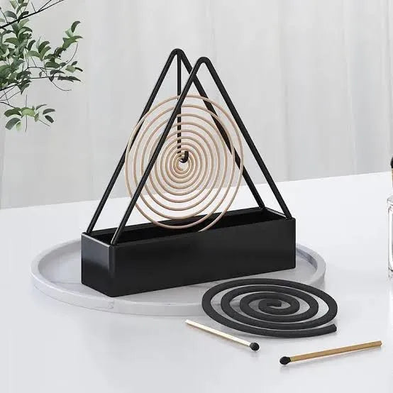 Black triangular incense holder with coiled incense on a white surface.