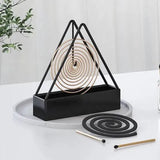 Black triangular incense holder with coiled incense on a white surface.