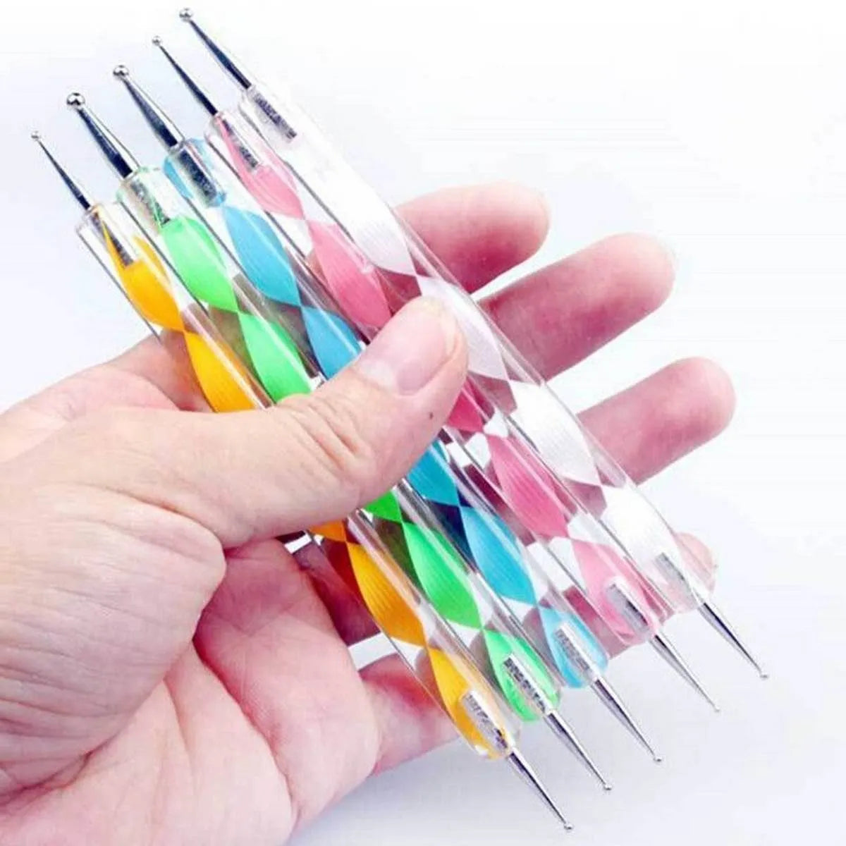 A hand holding a set of six clear acrylic nail art tools with colorful diamond-patterned handles in yellow, green, blue, pink, orange, and white, each tipped with a silver metal needle.