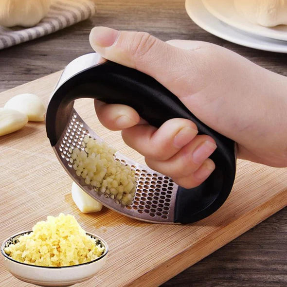 Hand using a garlic press on a wooden cutting board with minced garlic and whole garlic cloves.
