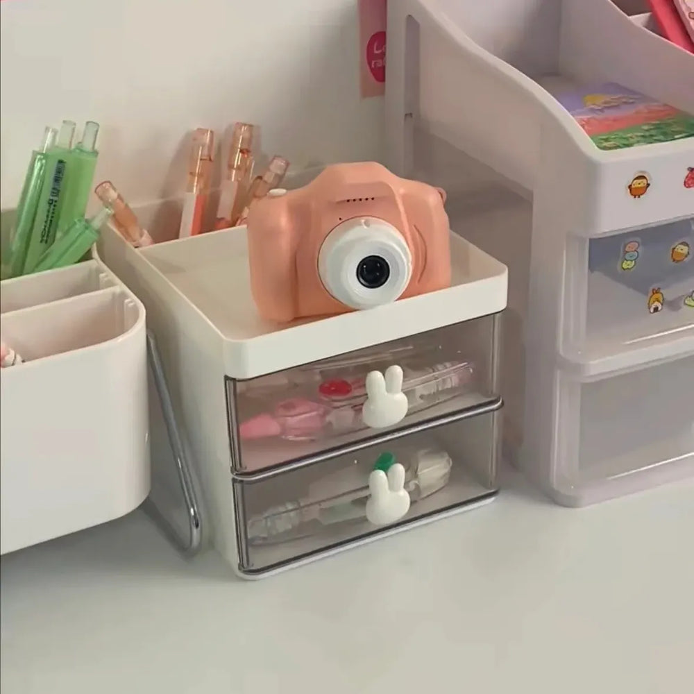 Pink camera on a transparent drawer with stationery items in a well-organized desk setup.