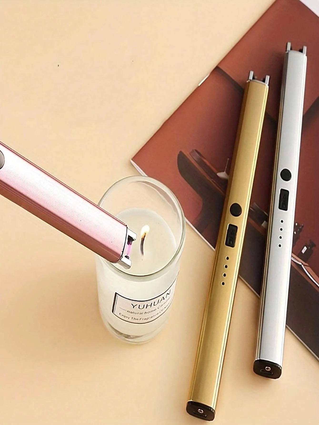 Three electronic devices on a beige surface with a candle and magazine in the background.