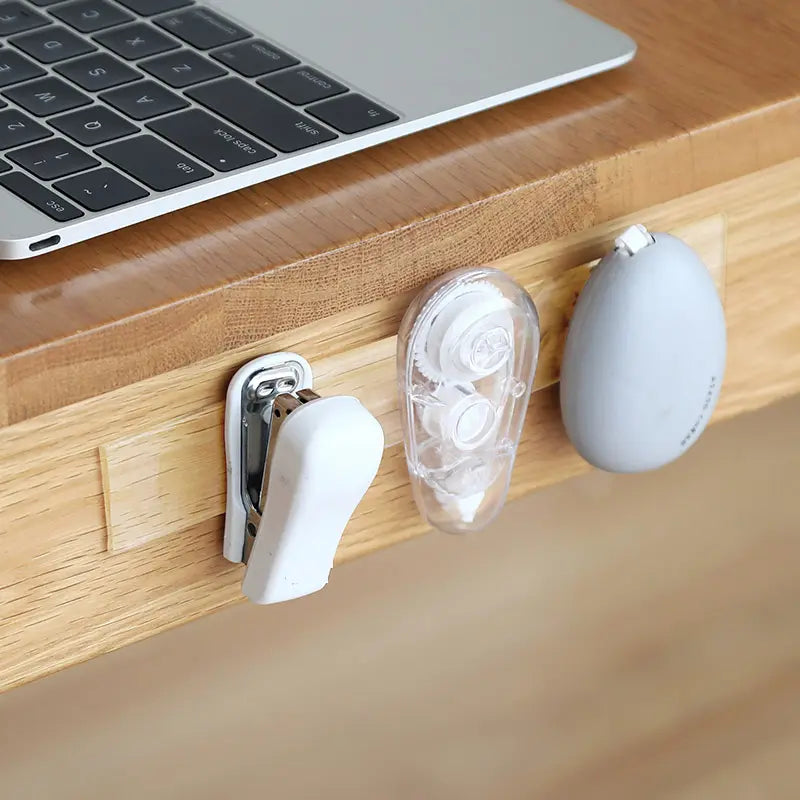 Desk with laptop, earbuds, and a white cable management product on a wooden surface.