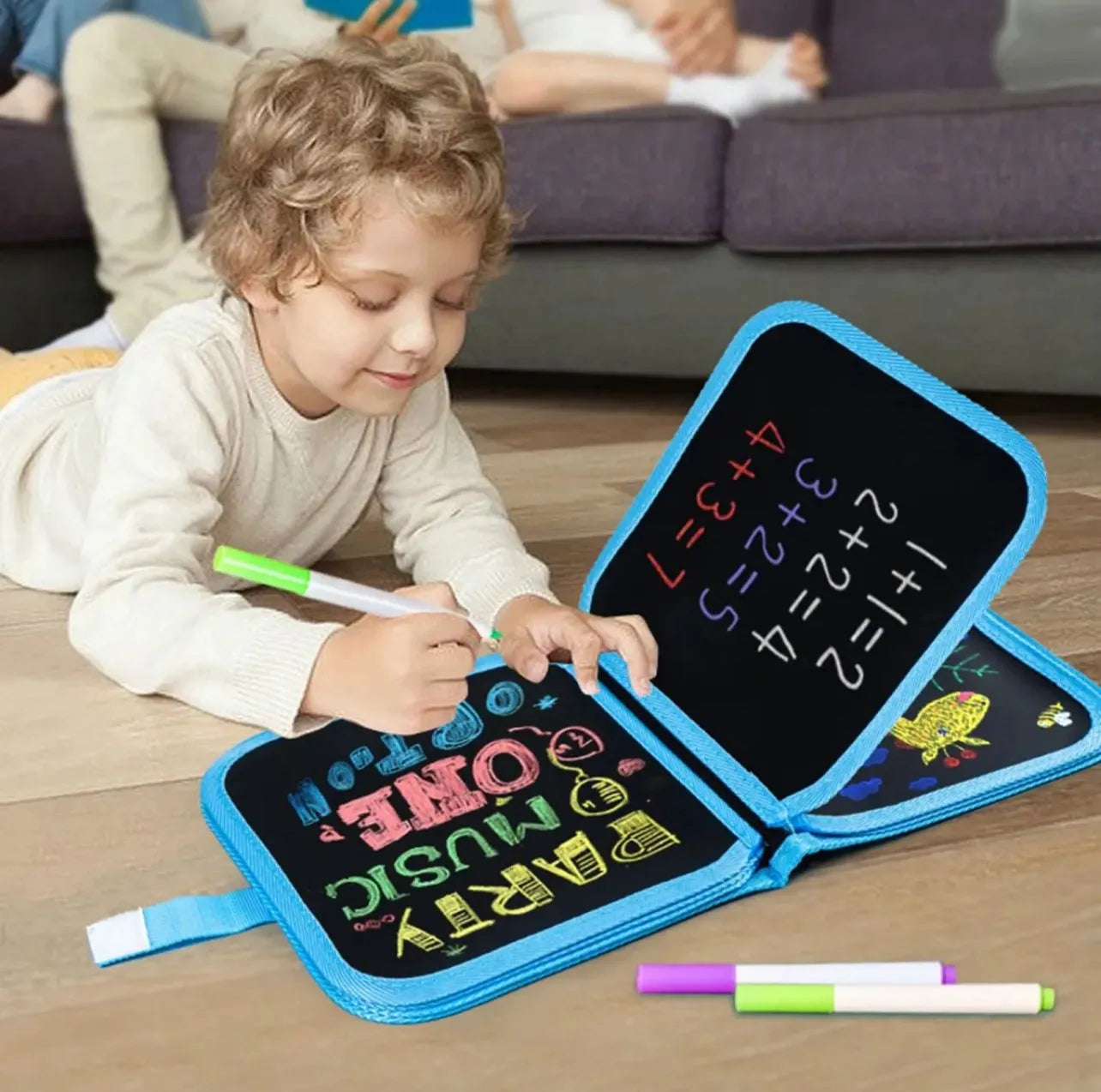 Child playing with a portable blackboard and markers on a wooden floor.