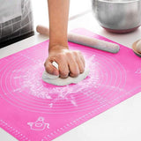 Person kneading dough on a pink baking mat with a rolling pin
