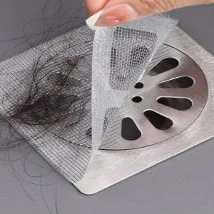 Hair trapped in a mesh drain cover with a hand holding it above a sink drain.
