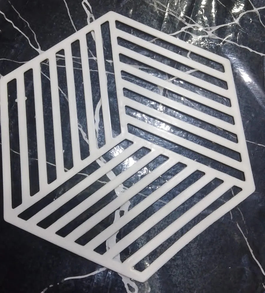 A white plastic hexagonal guard grille or safety guard with diagonal and parallel slotted patterns, shown on a dark marble surface.