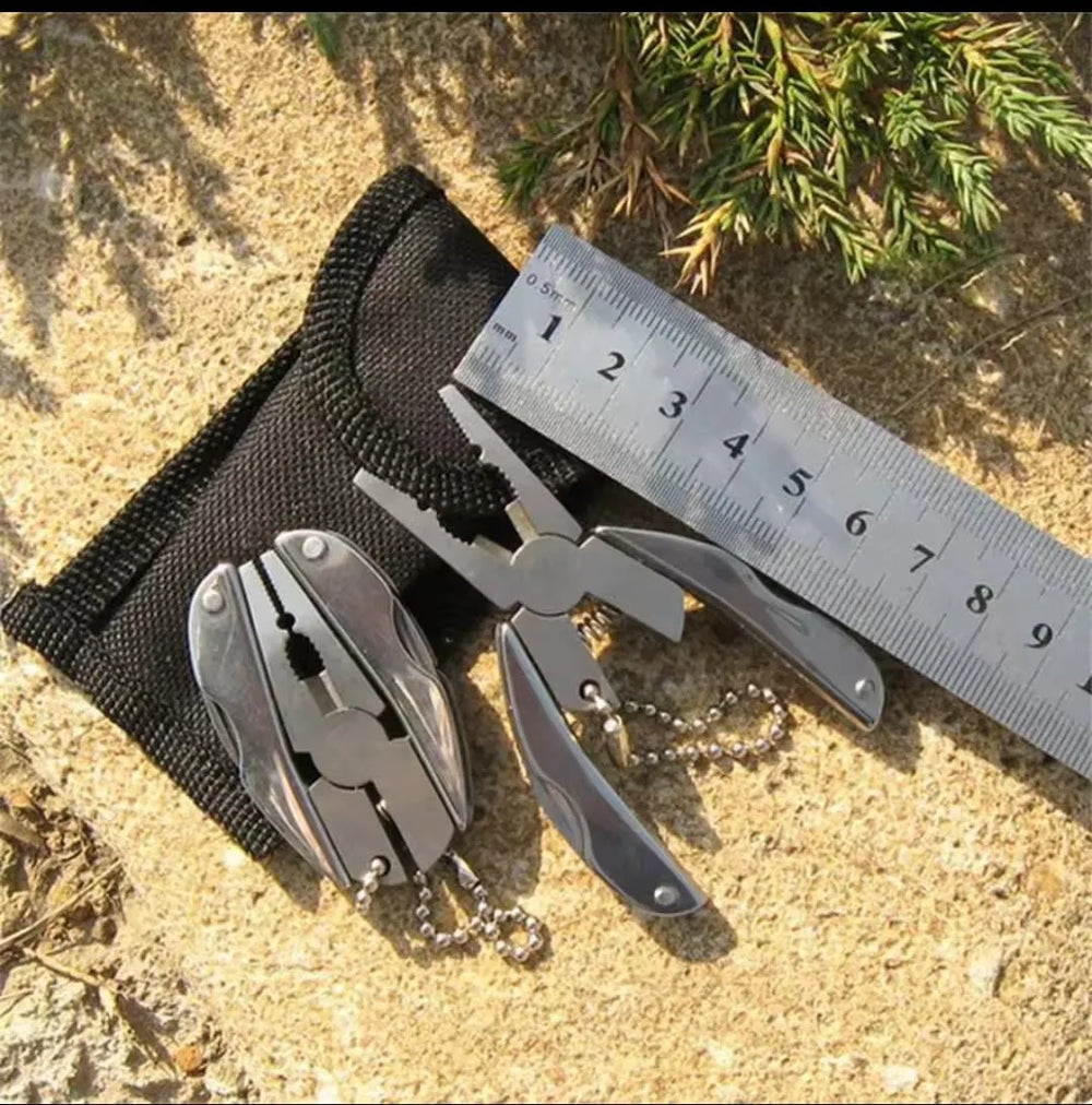 Multitool with pliers and cutters on a sand surface with a ruler for scale