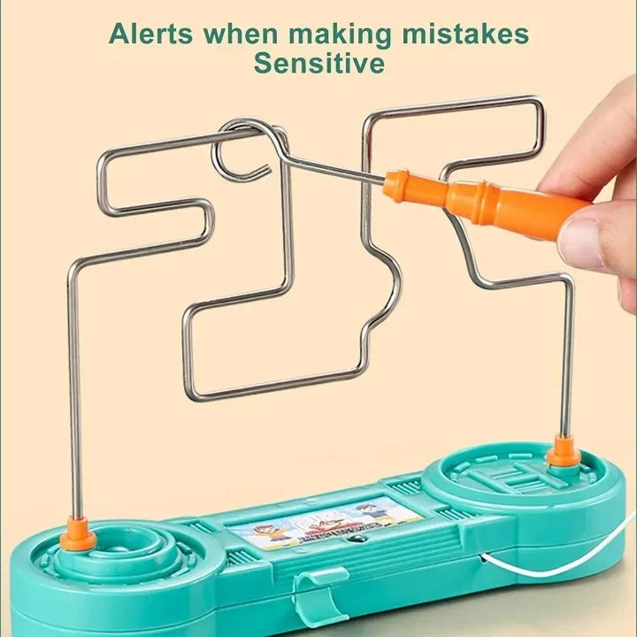 A metal maze toy on a teal plastic base with orange handles, shown with a hand guiding a metal probe along the path. Text at the top reads 'Alerts when making mistakes Sensitive'.