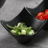 Black ceramic bowl with two compartments, one filled with green salad and the other with red cherry tomatoes.