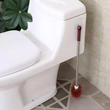Toilet cleaning brush with red bristle head leaning against a white toilet in a bathroom.
