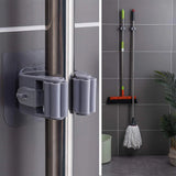Gray wall-mounted cleaning tool holder attached to a shower door with cleaning tools in the background.