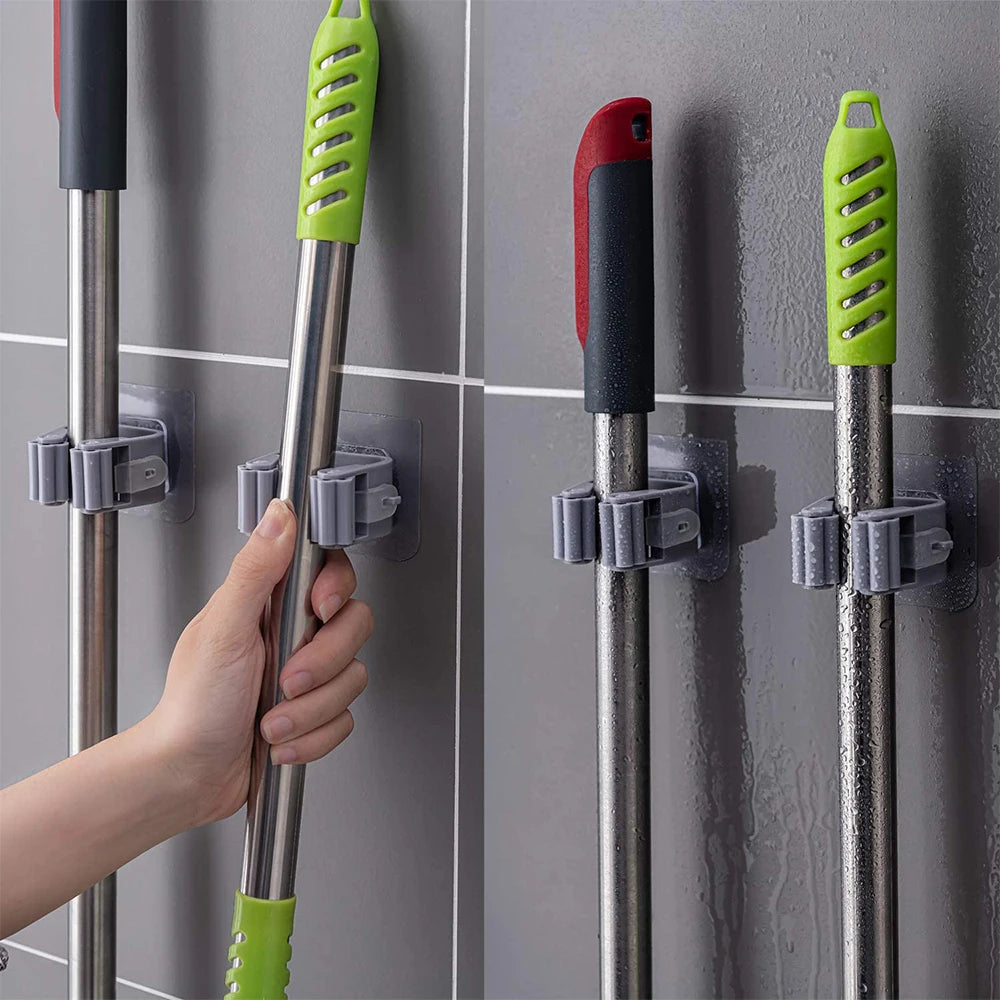 Mop and broom holders on a tiled wall with a hand holding a mop.