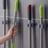 Mop and broom holders on a tiled wall with a hand holding a mop.